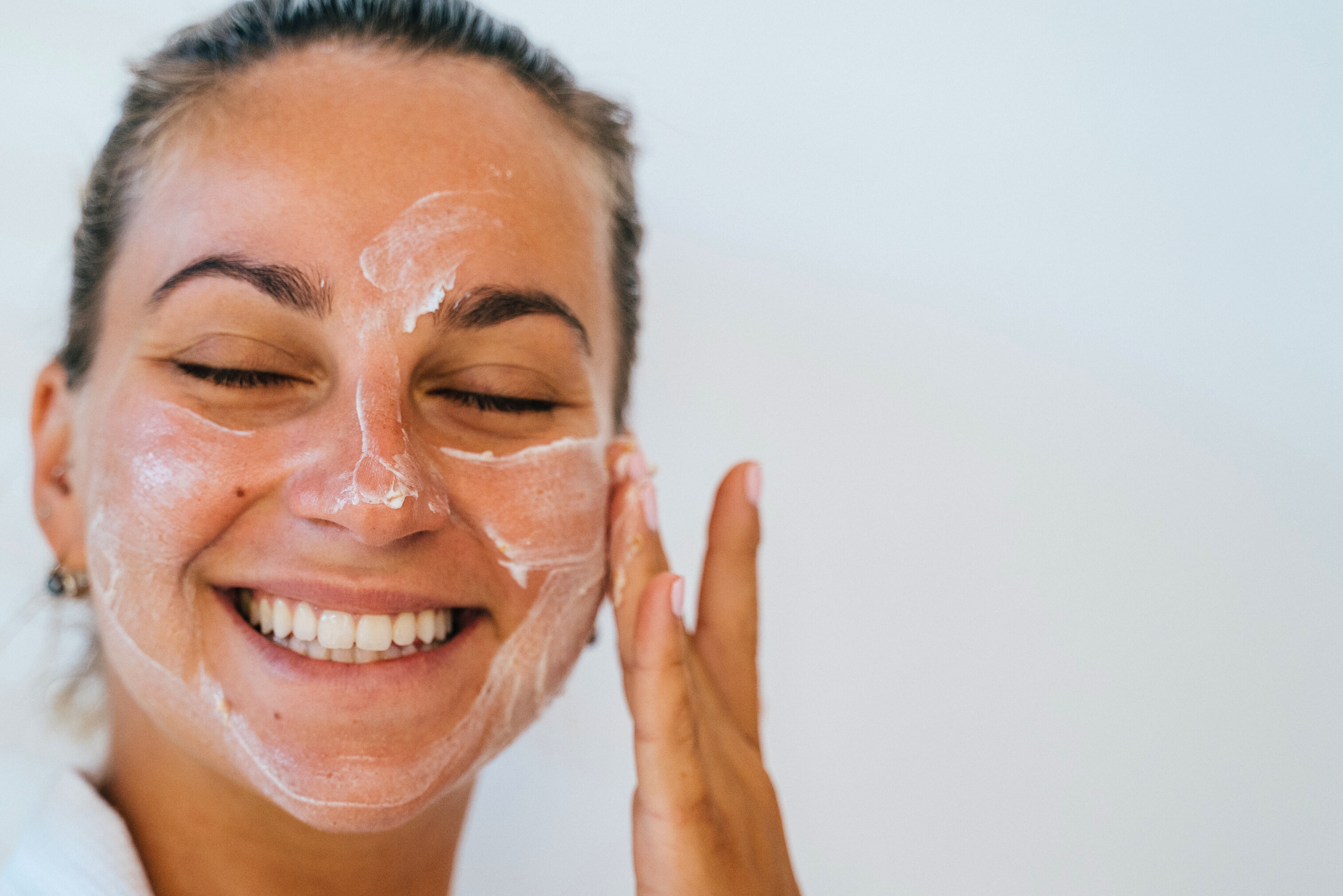 Woman applying a facial mask with a neutral background