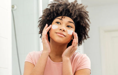 Woman in bathroom applying facial cream to cheeks