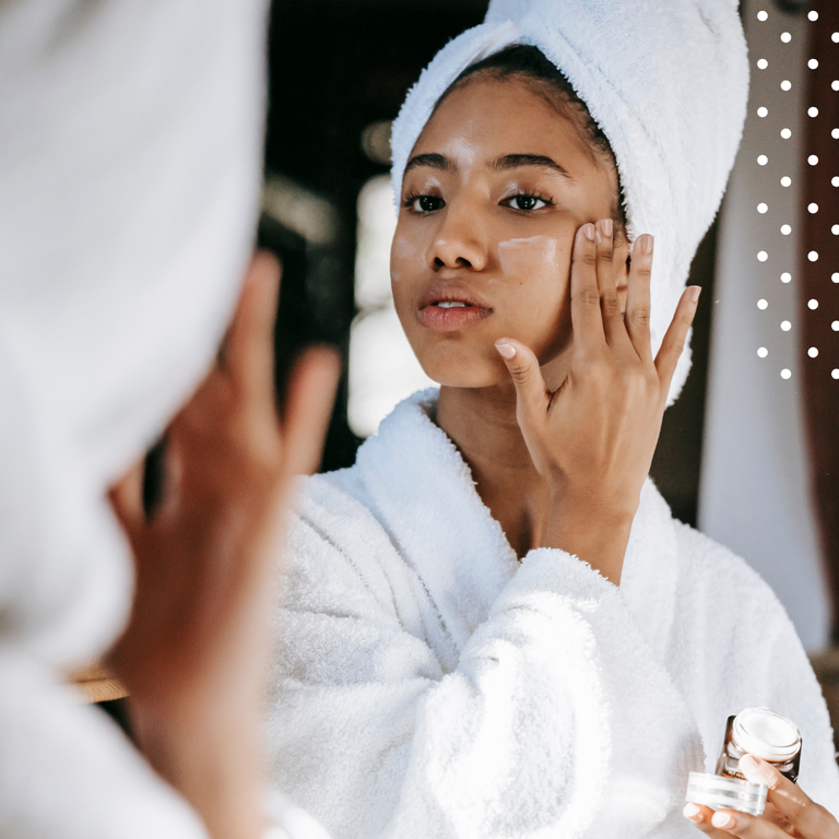Smiling woman using skincare cream in front of a mirror