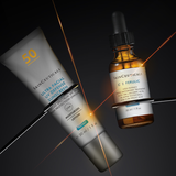 Two skincare products from SkinCeuticals are displayed on a dark background with dramatic light effects: a silver tube of Ultra Facial UV Defense Sunscreen SPF 50 and a brown glass dropper bottle of C.E Ferulic antioxidant treatment.